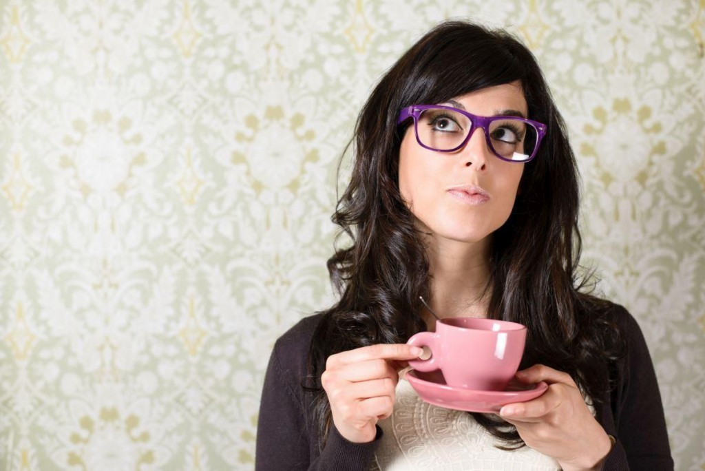 Casual woman thinking and looking pensive on retro vintage background. Brunette girl looking up and holding cup of coffee.