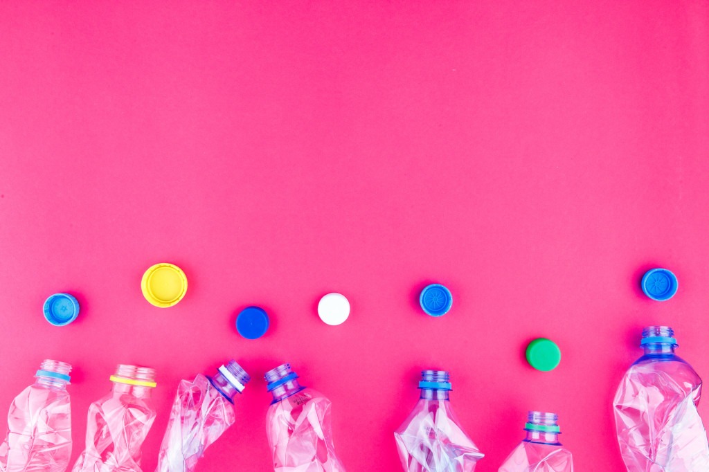 Four crushed PET bottles and colorful caps closeup on vivid pink purple background. Empty space. Plastic collection fashion attractive concept. Ecological poster template.